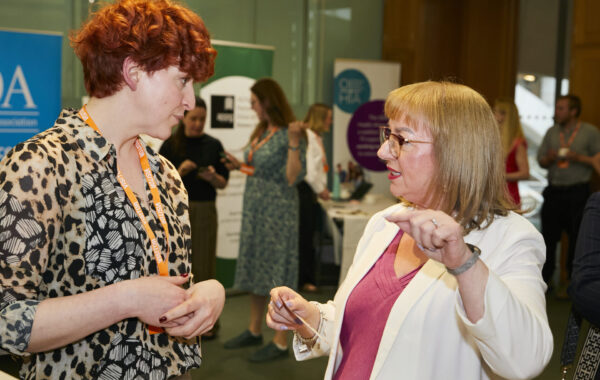 Corin, a white woman with red hair, talks to Sharon Hodgson MP, a white woman wearing a white jacket and red dress.
