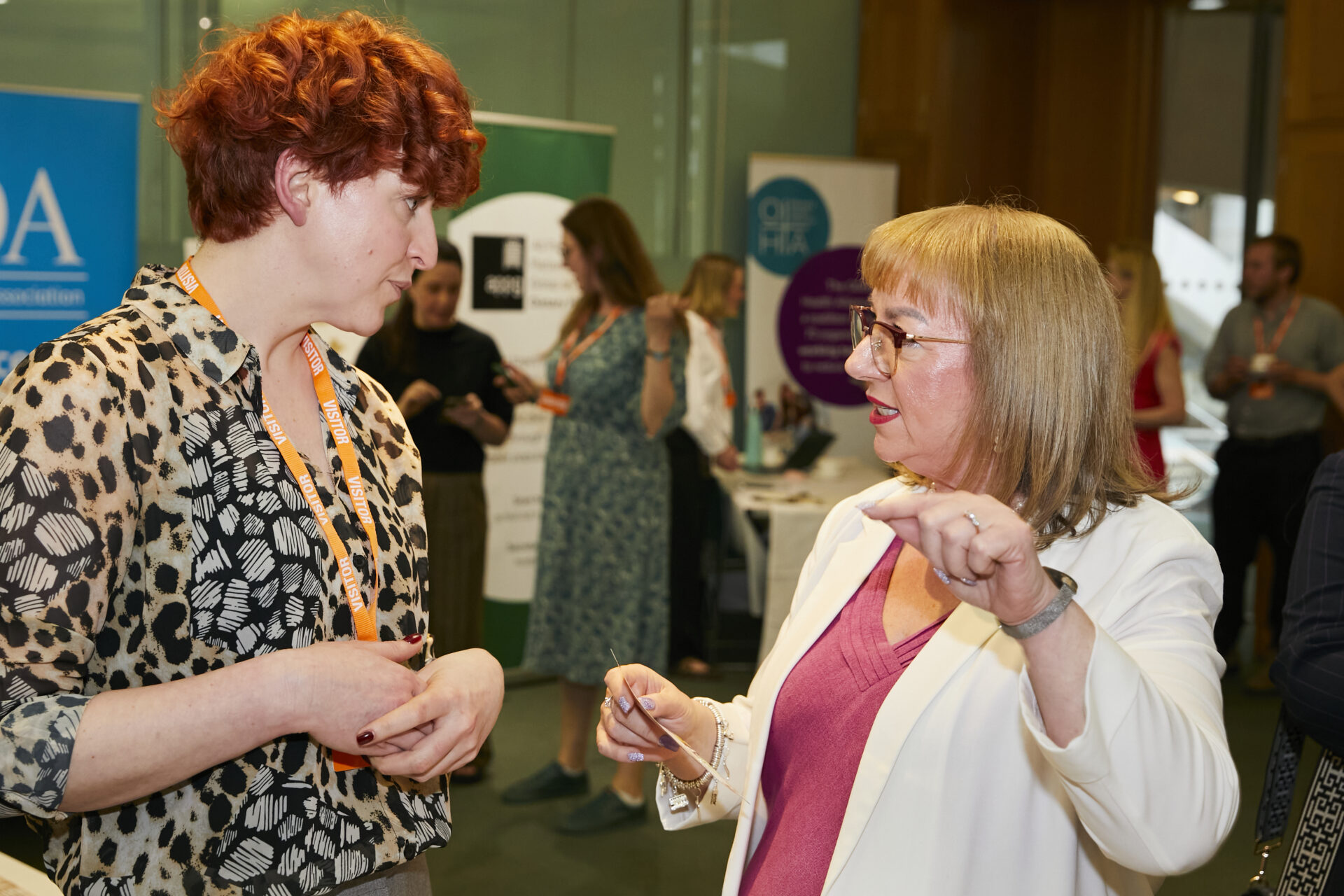 Corin, a white woman with red hair, talks to Sharon Hodgson MP, a white woman wearing a white jacket and red dress.